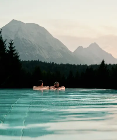 Couple relaxing in infinity pool with scenic mountain view at sunset